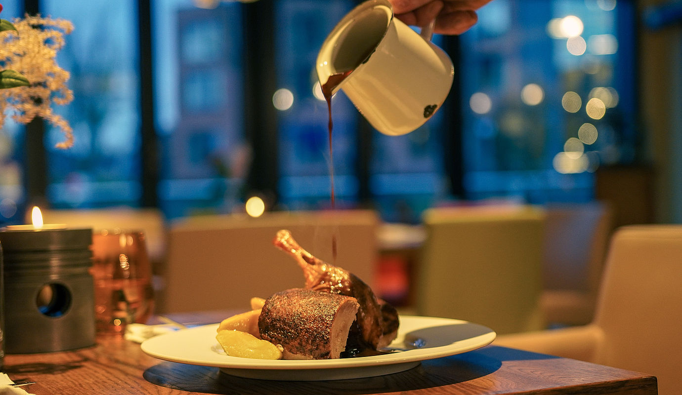 Entengericht mit Soße, Kartoffeln und Kerzenlicht im Restaurant.