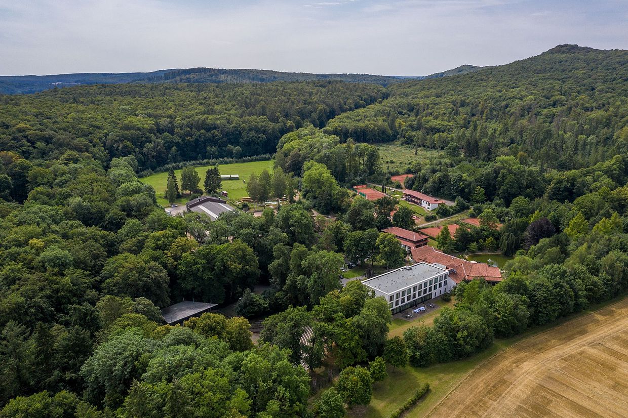 Eine Luftaufnahme des Hotel FREIgeist Northeim inmitten eines grünen, dichten Waldes in Niedersachsen