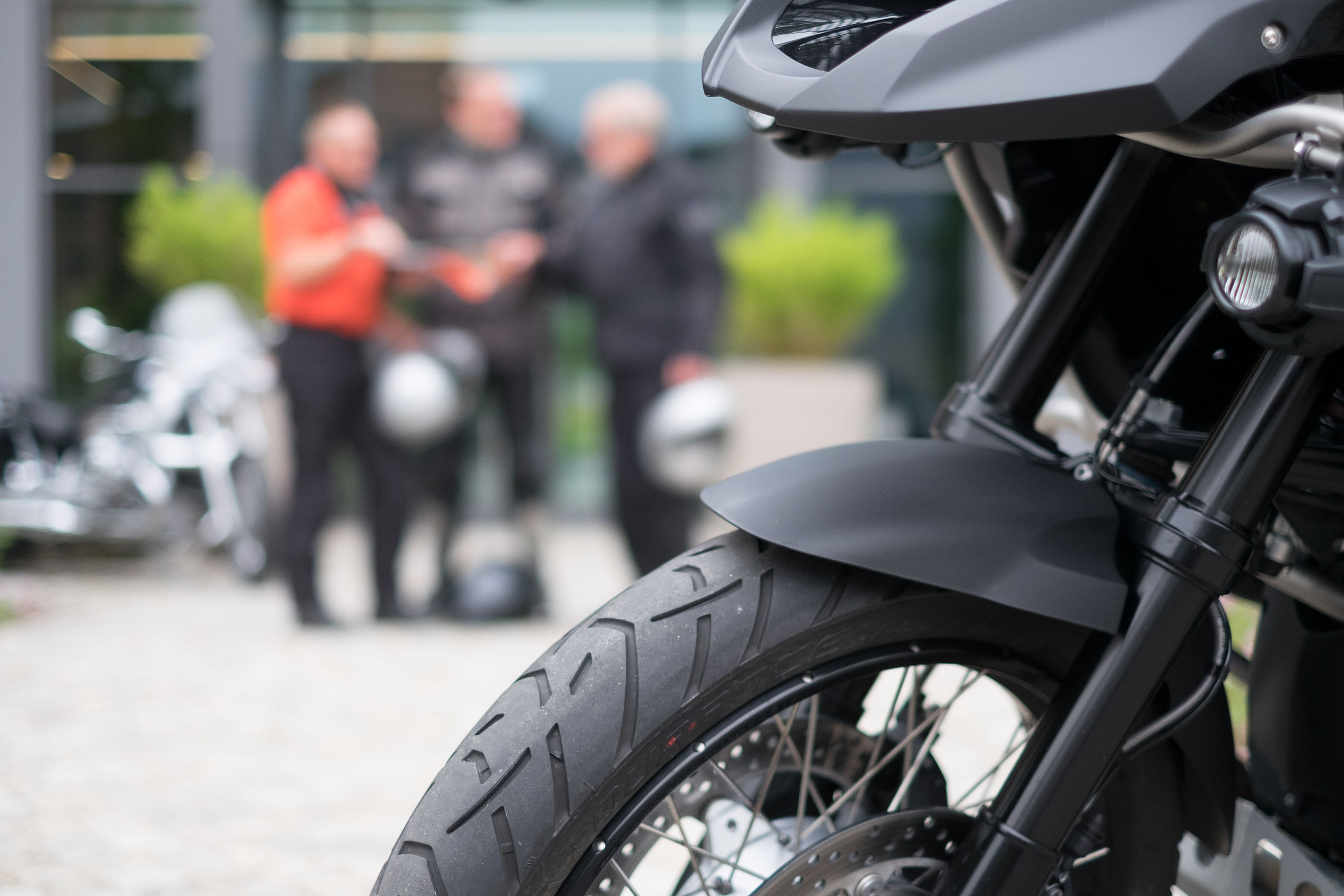 Fokus-Ausnahme von dem Vorderreifen eines Motorrads und im Hintergrund stehen drei Männer vor dem Eingang des Biker Hotels im Harz