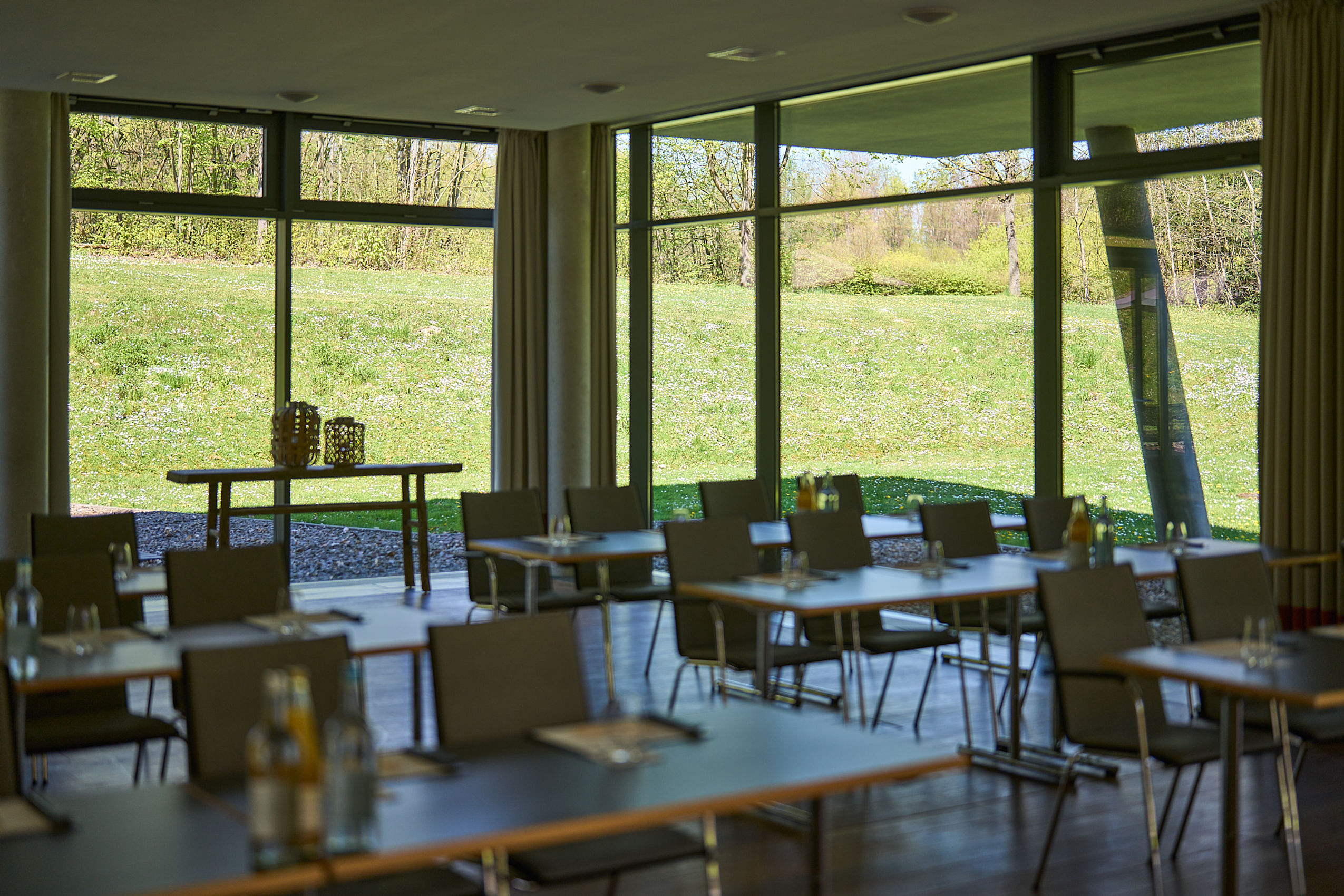 Mehrere Reihen von Tagungstischen im Saal mit großen Fenstern und Blick auf den Garten