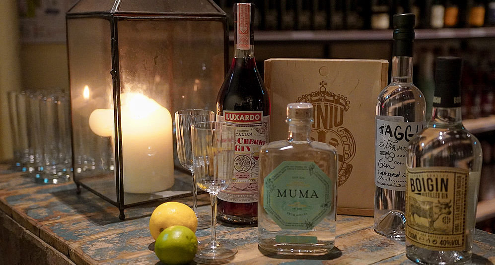 verschiedene Gin-Sorten auf einem Holzregal neben einer beleuchteten Kerze