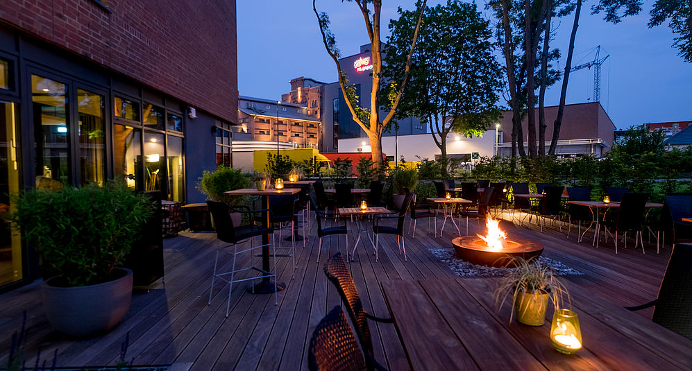 Blick auf die bestuhlte Holzterrasse mit brennender Feuerschale in der Mitte