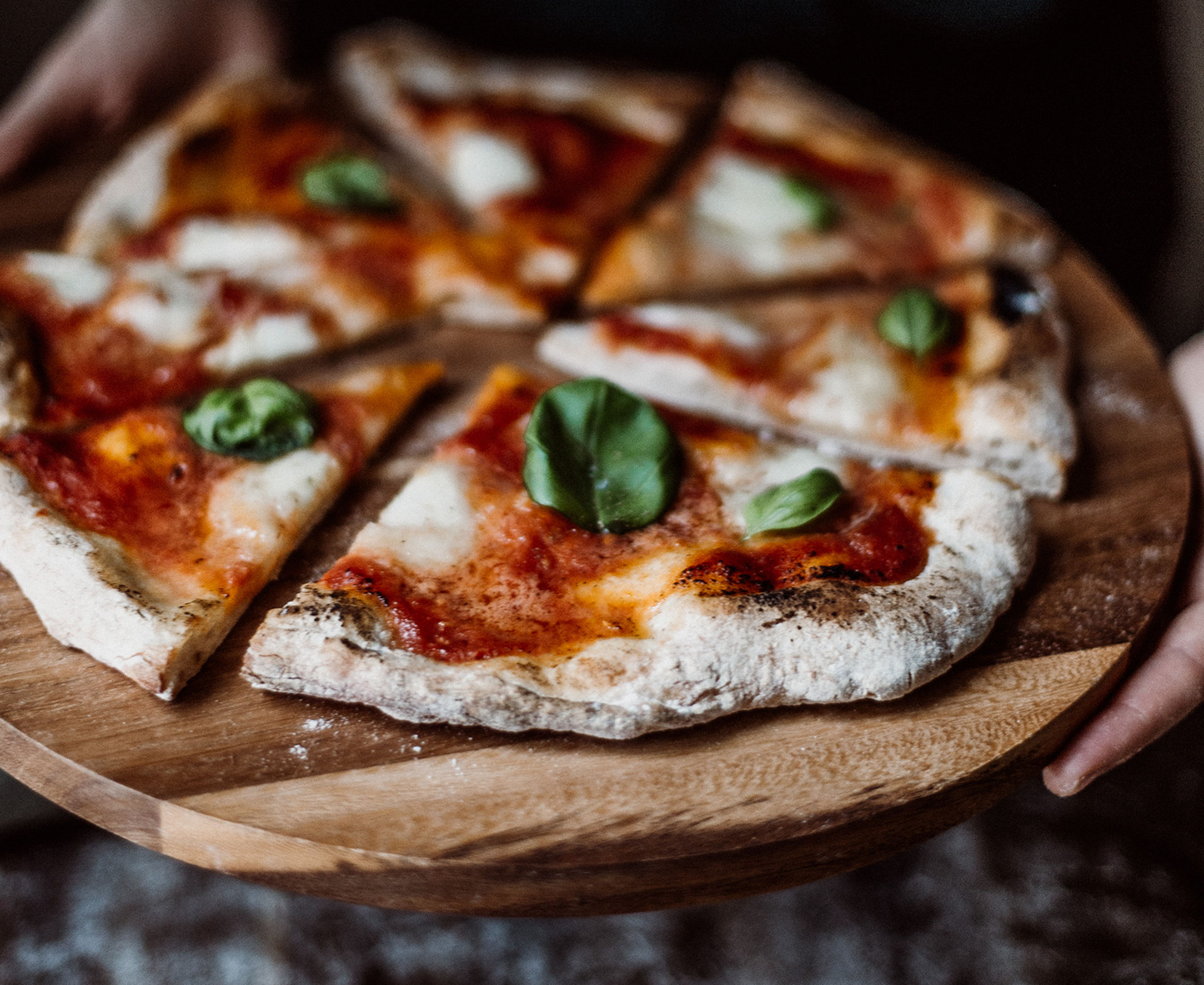 Eine Pizza Margharita mit Basilikumblättern auf einem Holztisch