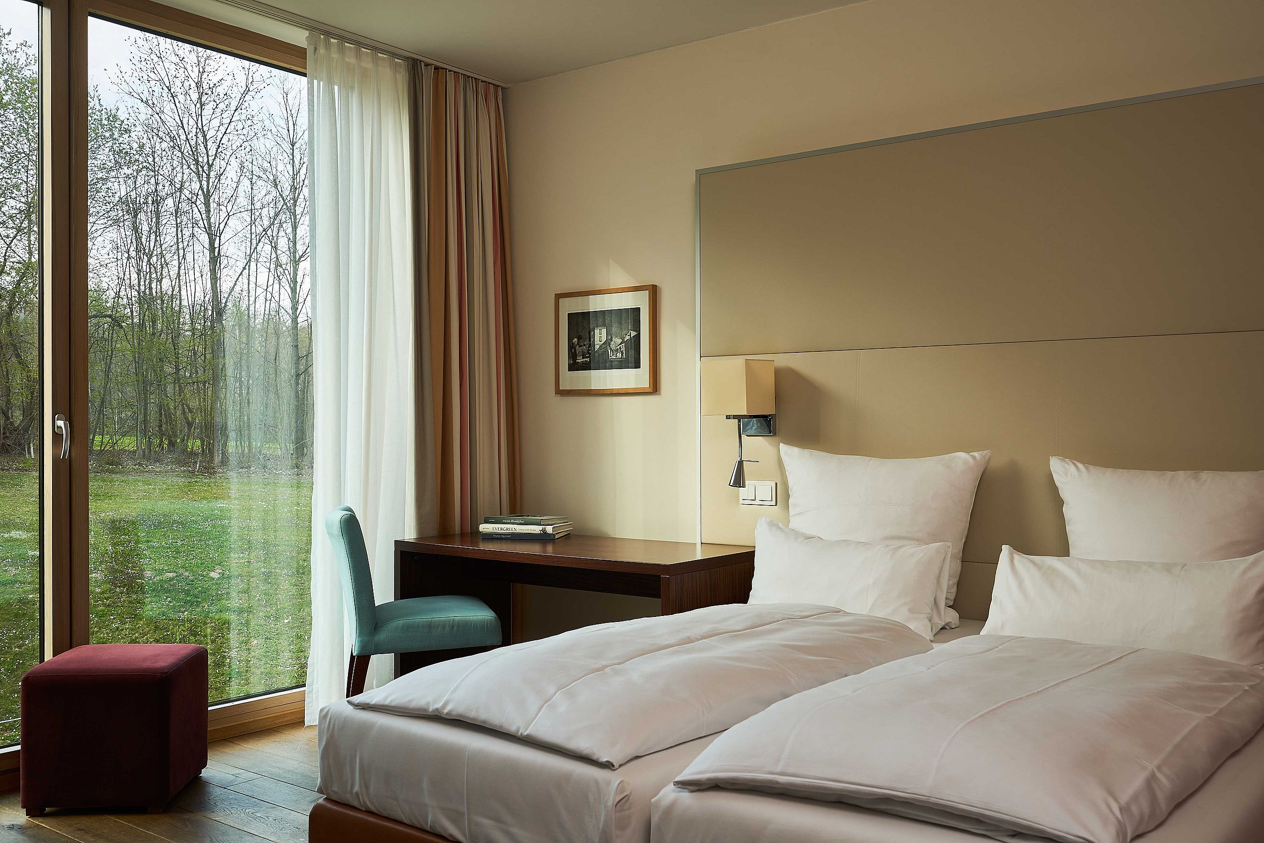 Ein frisch bezogenes Doppelbett mit Blick durch das Fenster in den Garten des Waldhotel FREIgeist Northeim