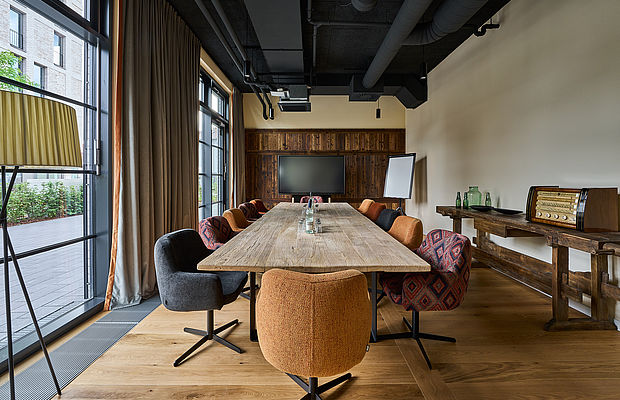 Langer Holztisch und bunte Stühle darum herum in einem Konferenzraum des FREIgeist Göttingen Nordstadt Hotels