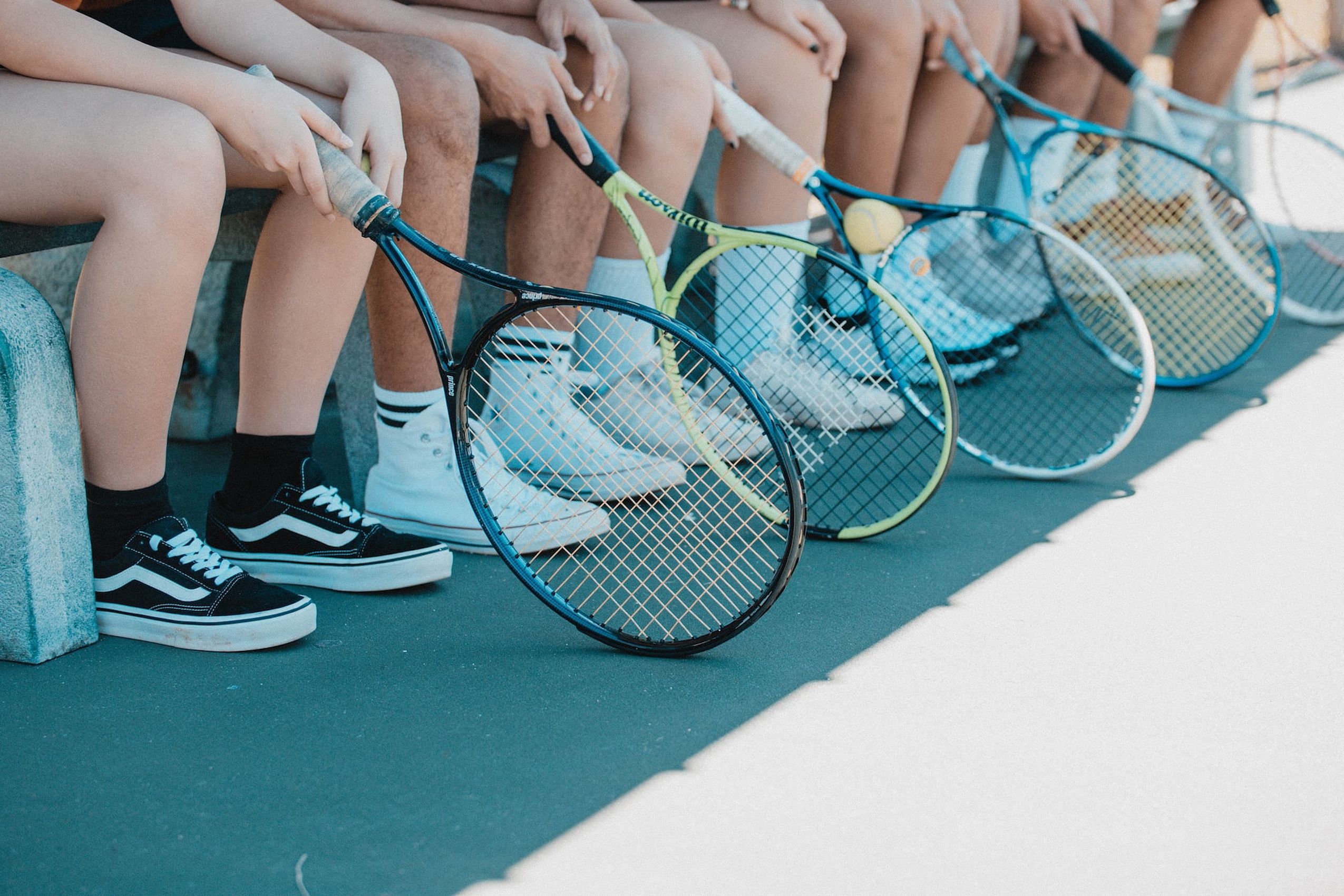 Mehrere Tennisspieler sitzen nebeneinander auf einer Bank und halten ihre Schläger in den Händen