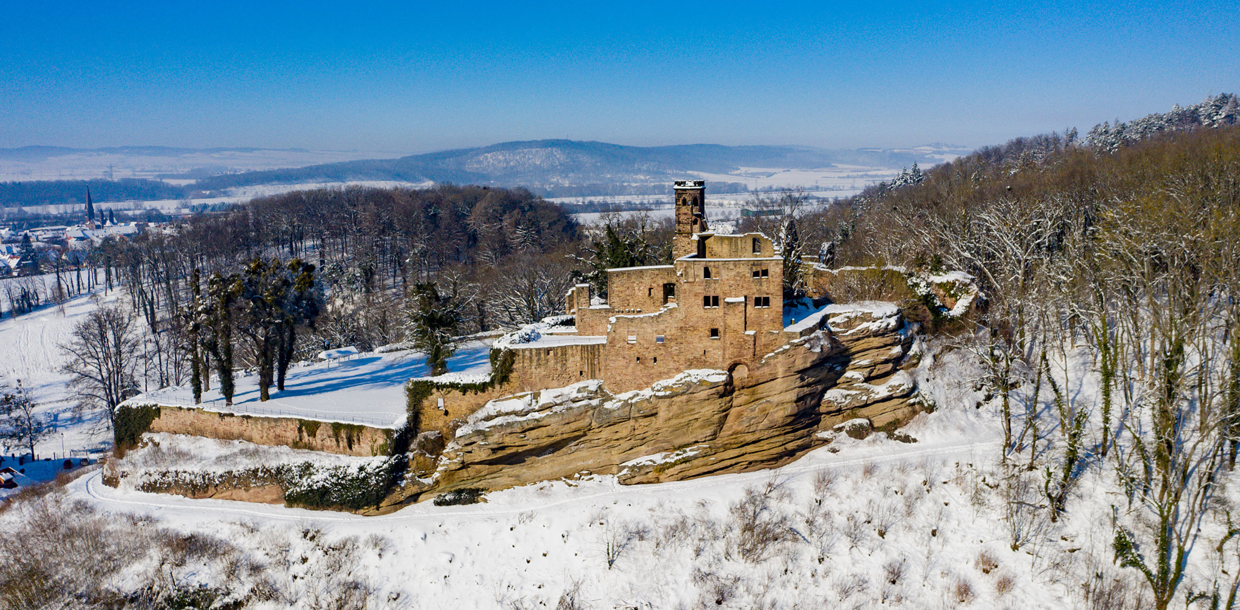 Luftaufnahme des Hardenberg BurgHotels im Winter mit schneebedeckter Landschaft und historischen Burgruinen.