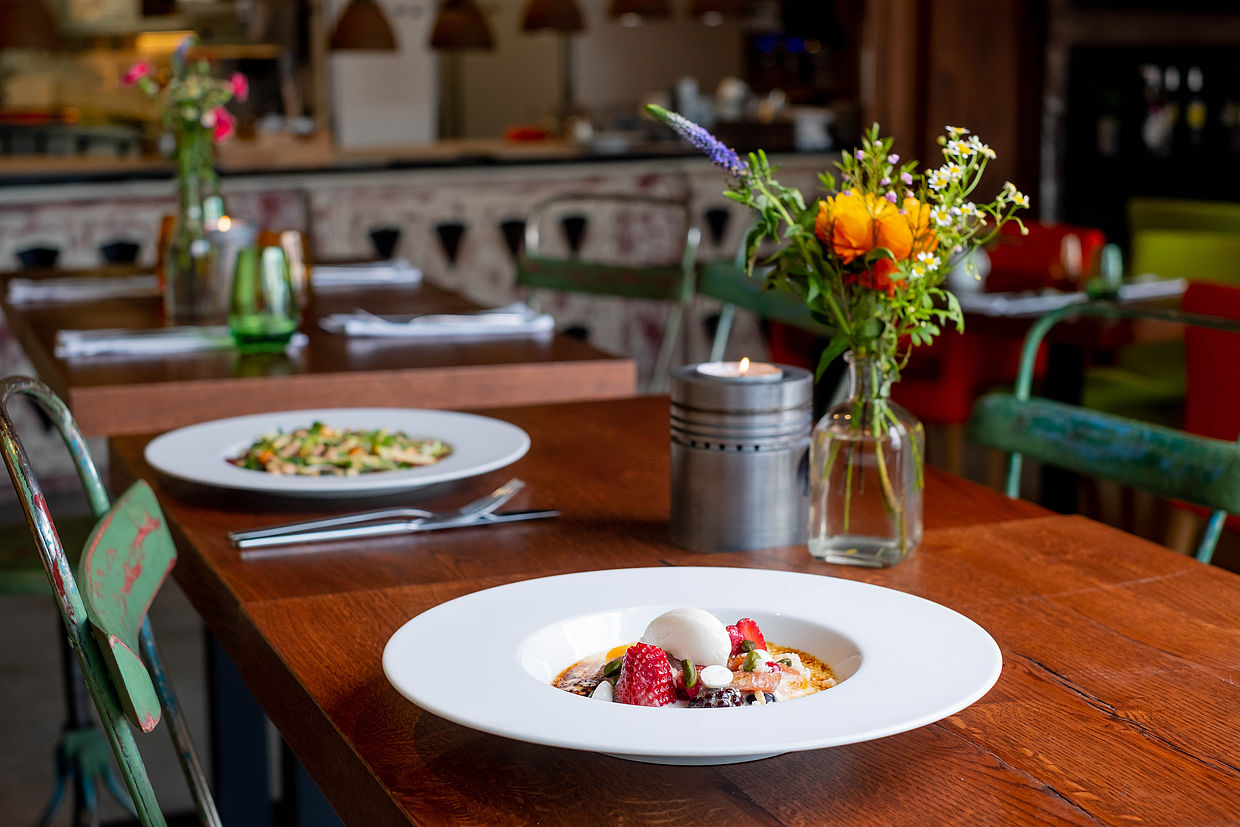 Zwei Gerichte stehen auf einem Tisch im Restaurant Einbeck, der mit einem Blumenstrauß und einer Kerze dekoriert ist