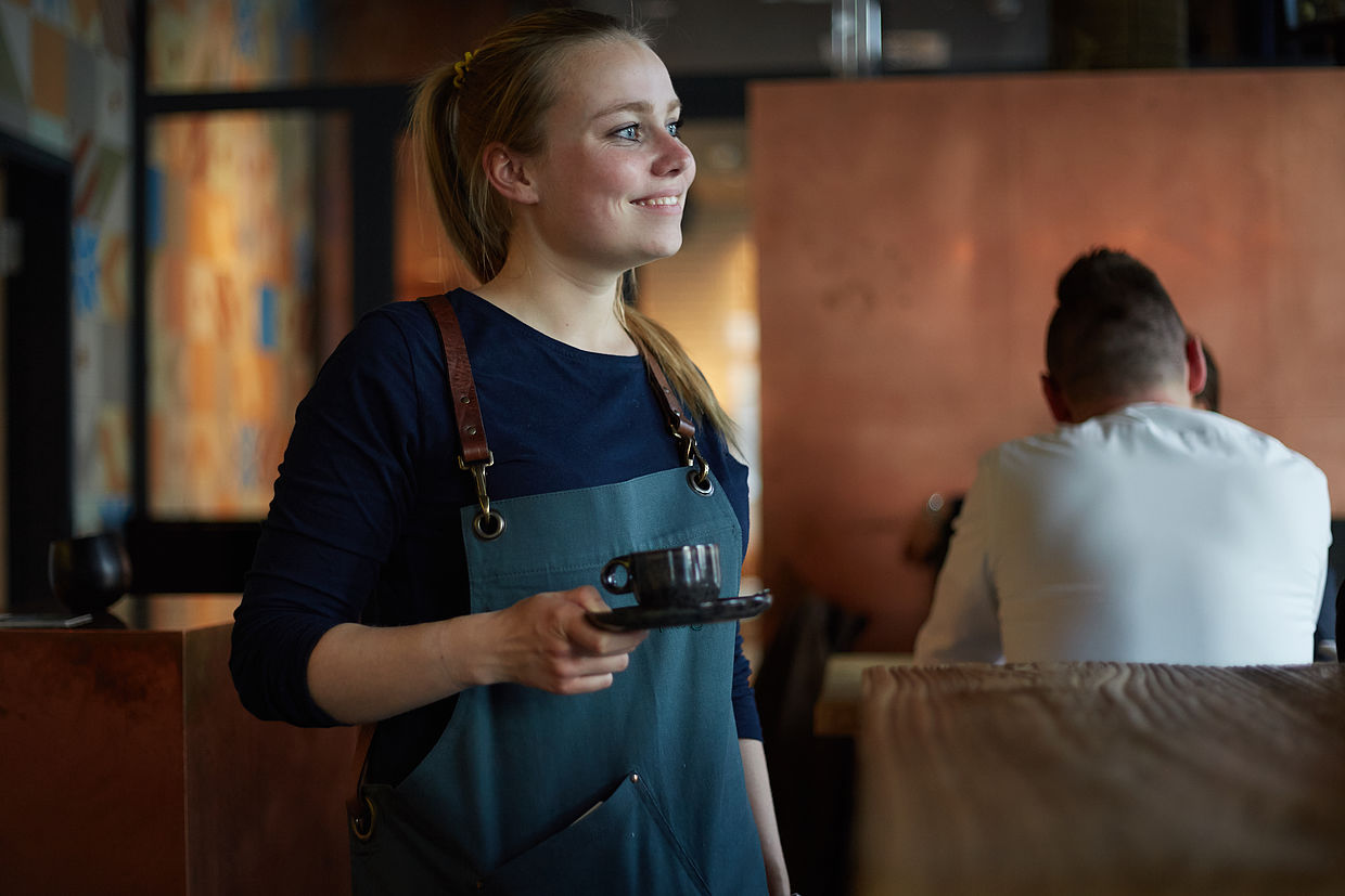 Eine Bedienung genießt Ihren Job im FREIgeist Göttingen Innenstadt und serviert lächelnd einen Kaffee