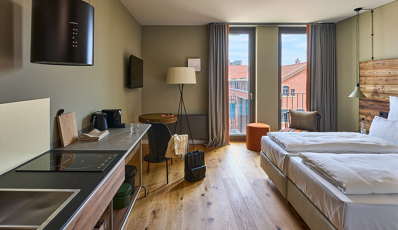 Einblick in ein Hotelzimmer im FREIgeist mit Doppelbett, Einbauküche und einem großen Fenster