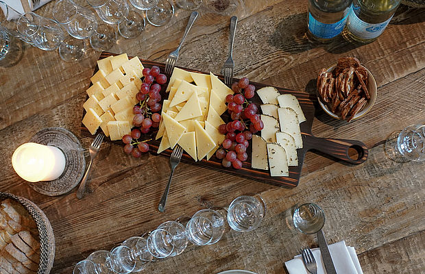 Vogelperspektive auf eine angerichtete Käse-Weintraube-Platte umrahmt von Tasting-Gläsern.