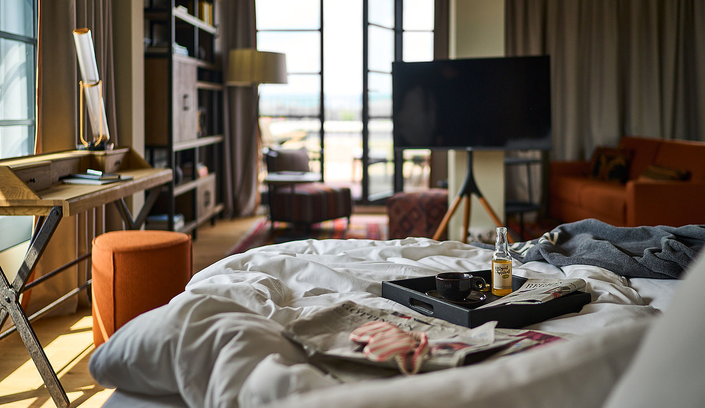 Ein Tablett mit Snacks und eine Zeitung liegen auf einem Bett im Hotel FREIgeist in Göttingen Nordstadt