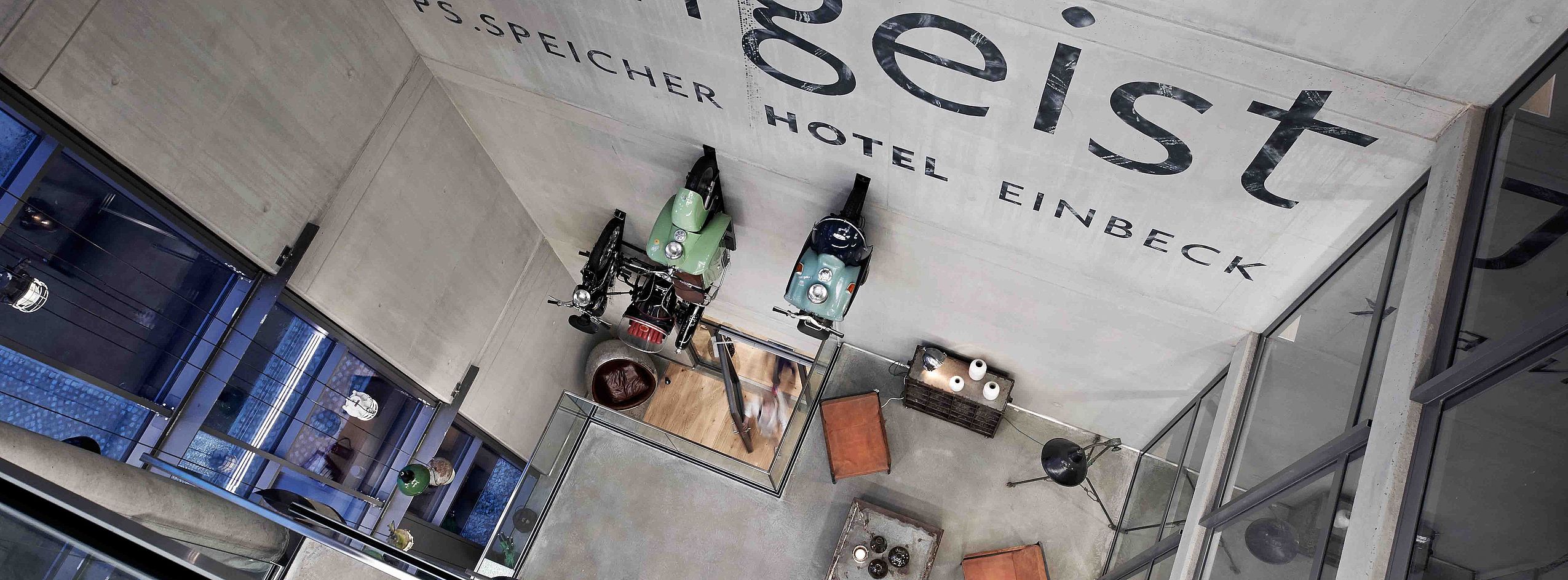 Blick von oben auf die Empfangshalle vom FREIgeist Einbeck, in der zwei Mofas an der Wand hängen