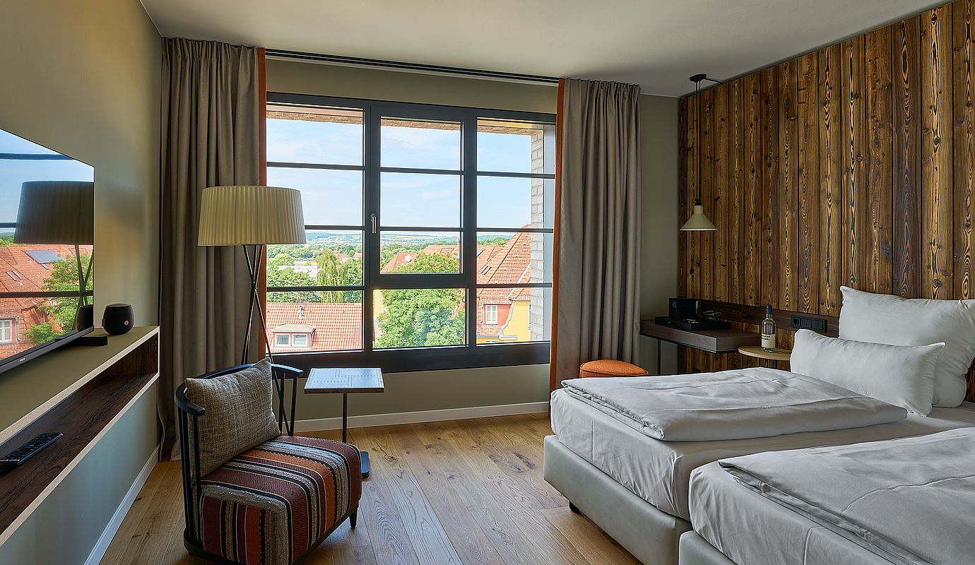 Blick auf ein helles Hotelzimmer mit großem Fenster und schönem Holzboden