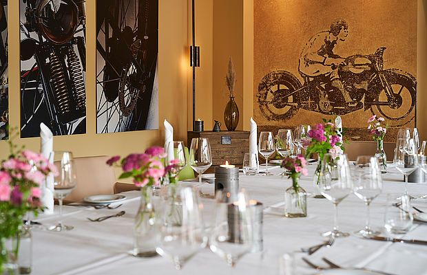 Eine lange Tafel ist in der Hochzeitslsocation in Hannover mit einer weißen Tischdecke eingedeckt und mit rosa-roten Blumen und Kerzen dekoriert