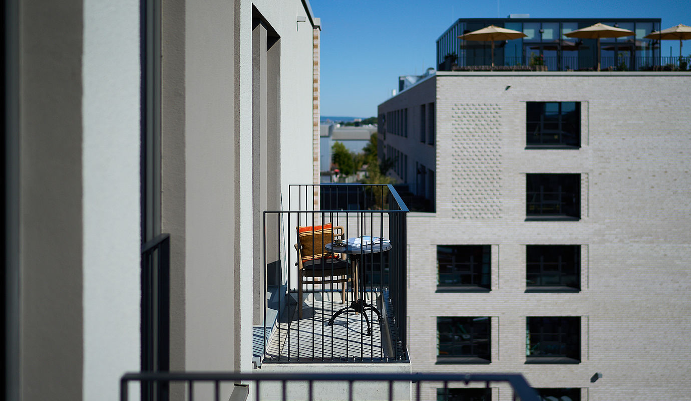 Seitlicher Blick auf einen Balkon mit einem gemütlichen, bunten Stuhl an der grauen Außenfassade des Hotels