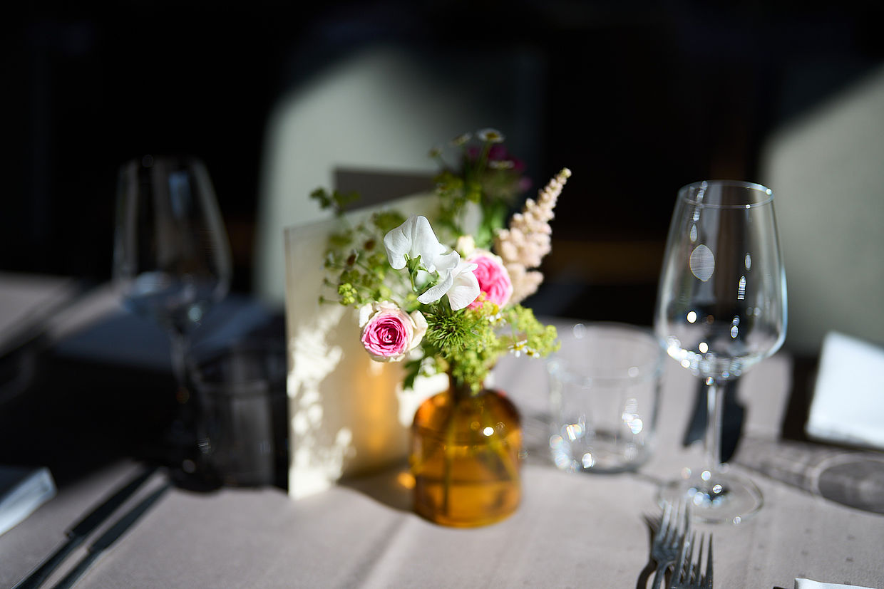 Detailaufnahme einer bunten Blumen-Tischdekoration zwischen zwei Weingläsern