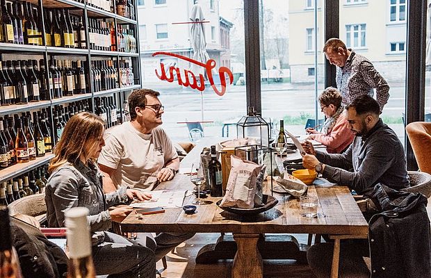 5 Personen stehen bzw. sitzen im Viani Alimentari an einem Holztisch und studieren Inhalte. 