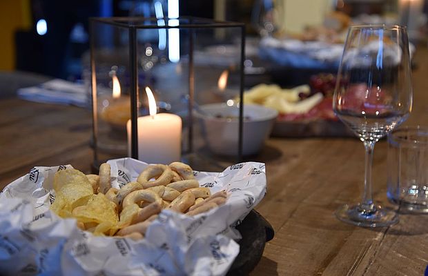 Weinglas und Chips vom Viani auf einem Holztisch neben einer leuchtenden Kerze. 