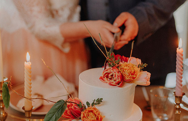 [Translate to english:] Hochzeitspaar schneidet minimalistisch dekorierte Hochzeitstorte an