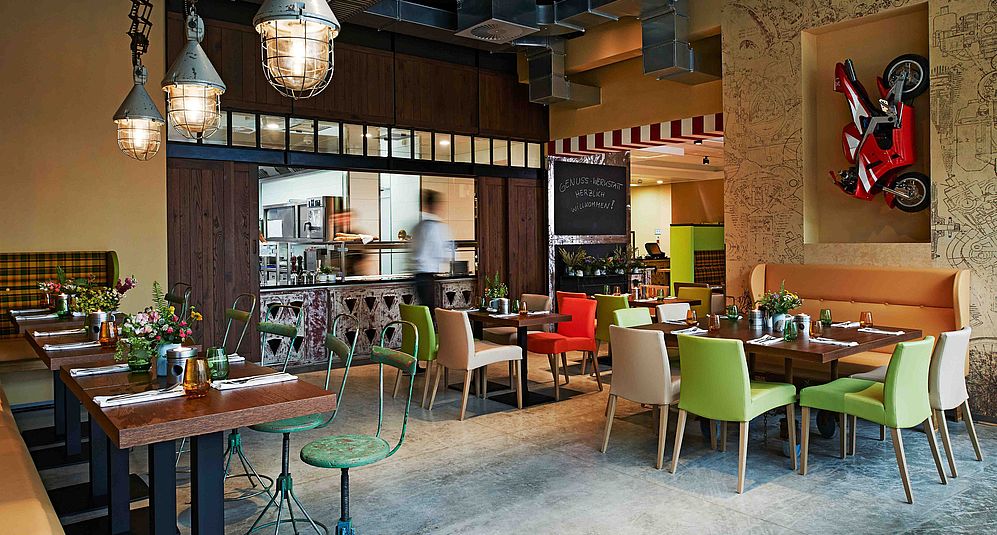 Restaurant im Design Hotel Hannover mit offener Küche, bunten Stühlen und eingedeckten Tischen
