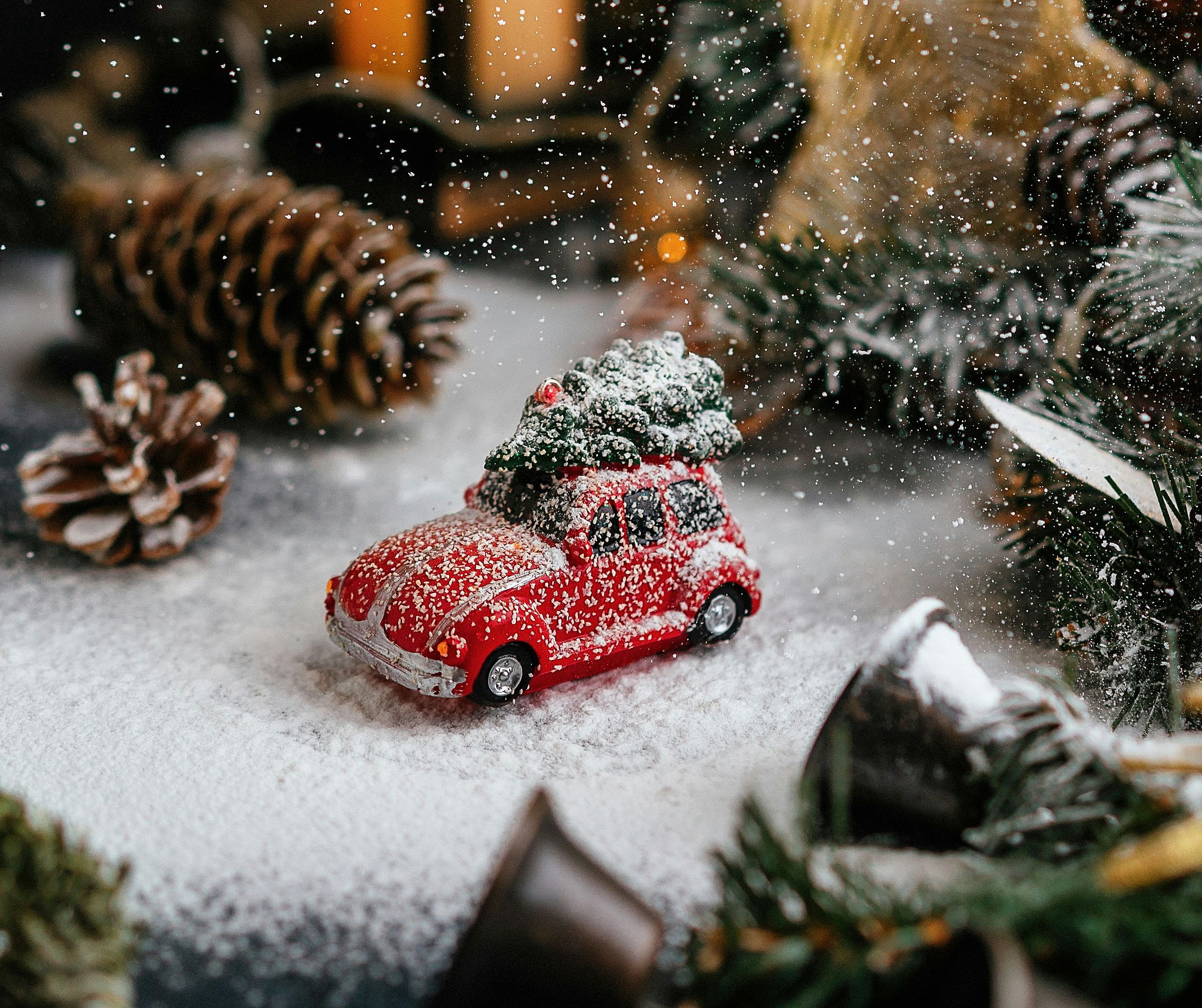 Nahaufnahme eines kleinen roten Spielzeugautos, das mit Schnee bedeckt und von Tannenzapfen umgeben ist