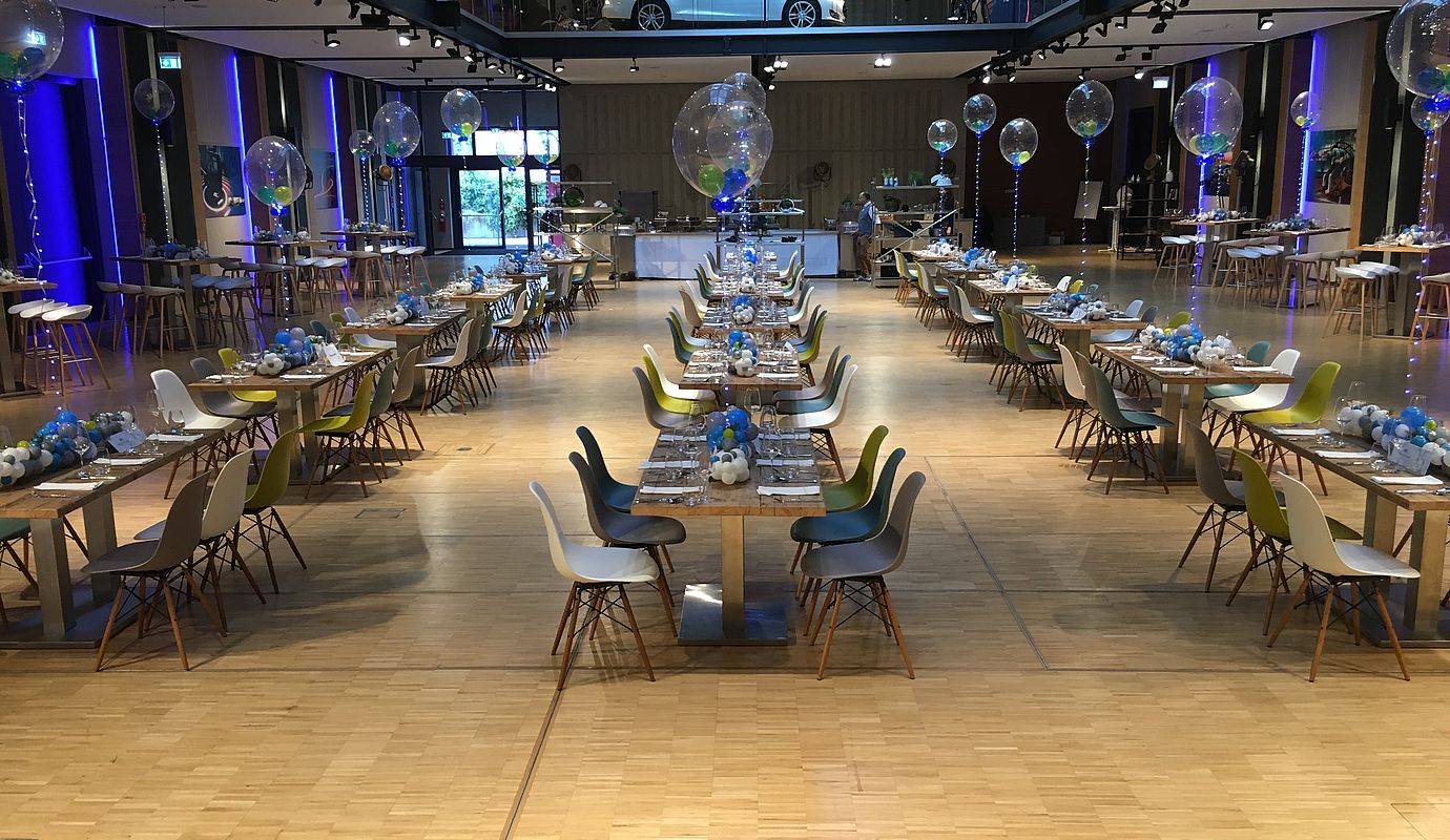 Große Eventhalle mit eingedeckten Tischen und schwebenden Luftballons