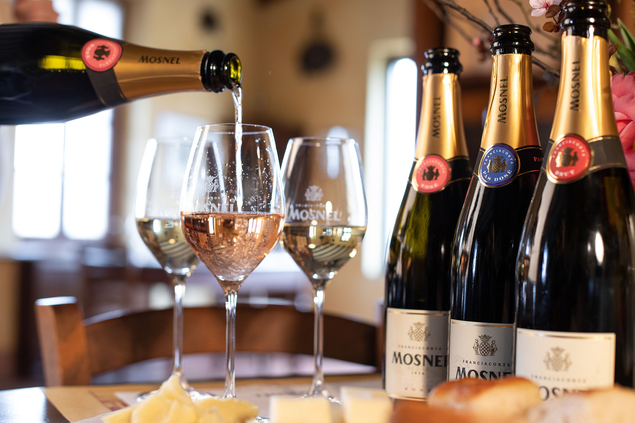 Champagner der Marke Mosel wird vor 3 Champagnerflaschen in ein Glas gekippt