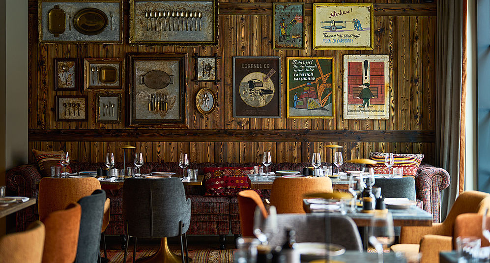 Mehrere gedeckte Tische und eine hohe Wand mit verschiedenen Bildern im Restaurant des FREIgeist Hotels in Göttingen