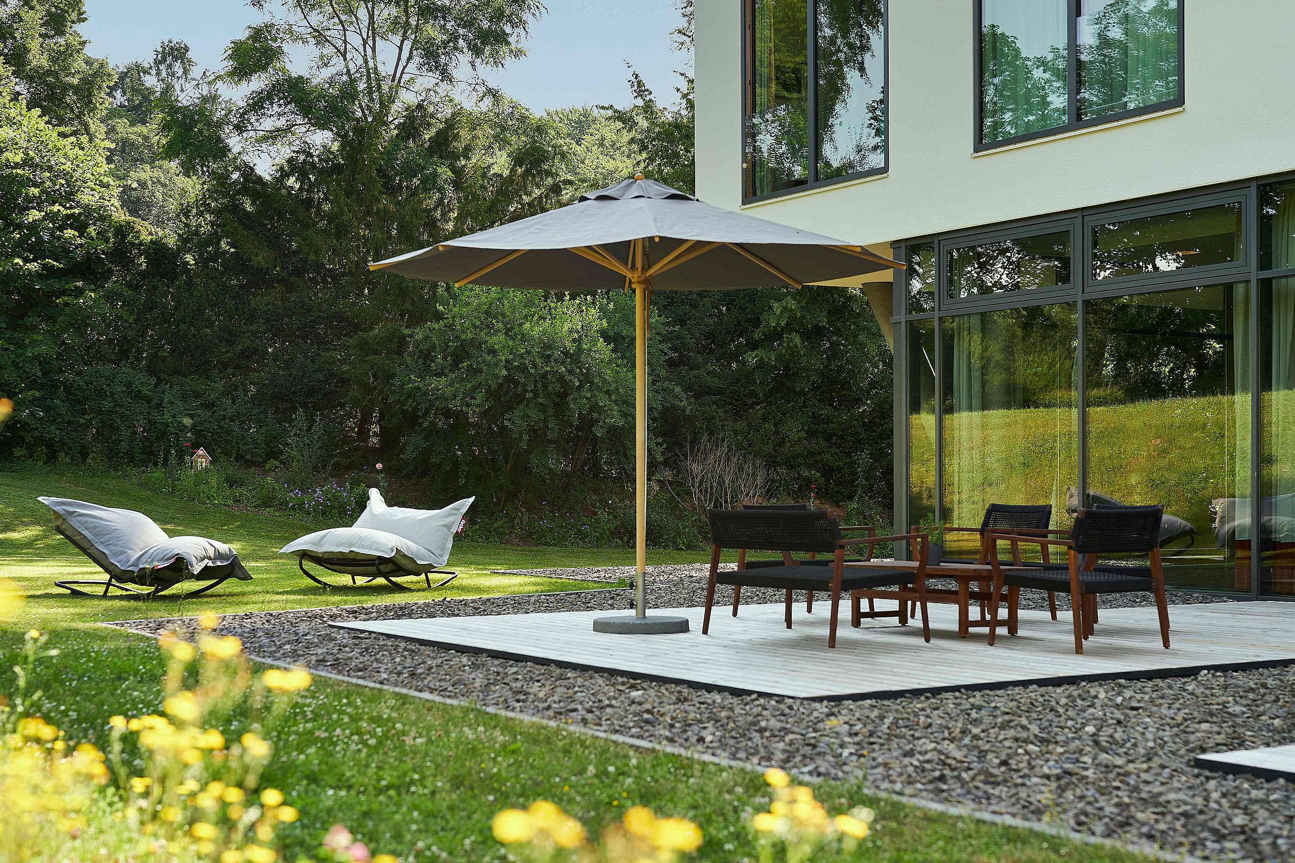 Eine moderne Terrasse im Waldhotel FREIgeist Northeim mit einem großen Sonnenschirm, einem Tisch und zwei bequemen Liegen