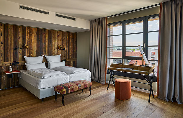 Ein Doppelbett und ein Schreibtisch neben einem großen Fenster in einem hellen Hotelzimmer
