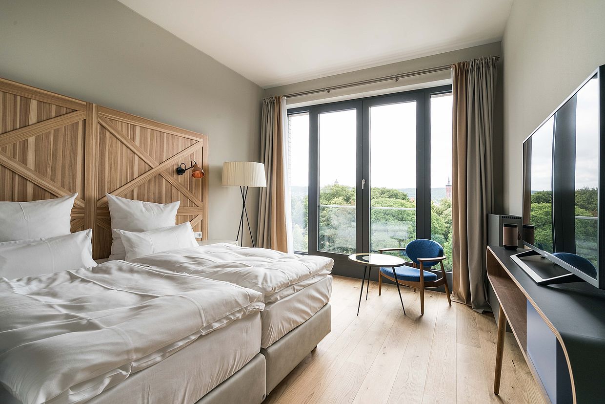 Ein frisch bezogenes Doppelbett in einem großen, hellen Hotelzimmer