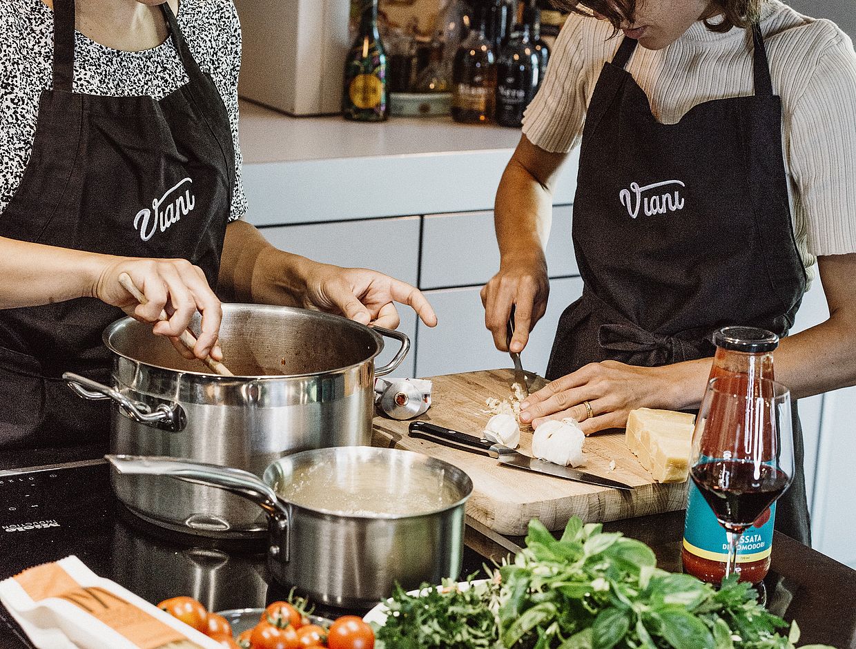 Zwei Personen in Viani-Schürzen stehen in einer Küche und kochen.
