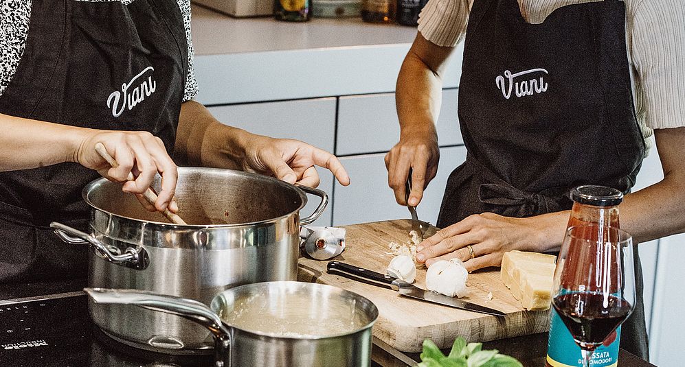 Zwei Personen in Viani-Schürzen stehen in einer Küche und kochen.