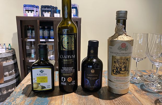 Verschiedene Olivenölsorten auf einem Holzregal im Viani Alimentari aufgereiht für ein Tasting 