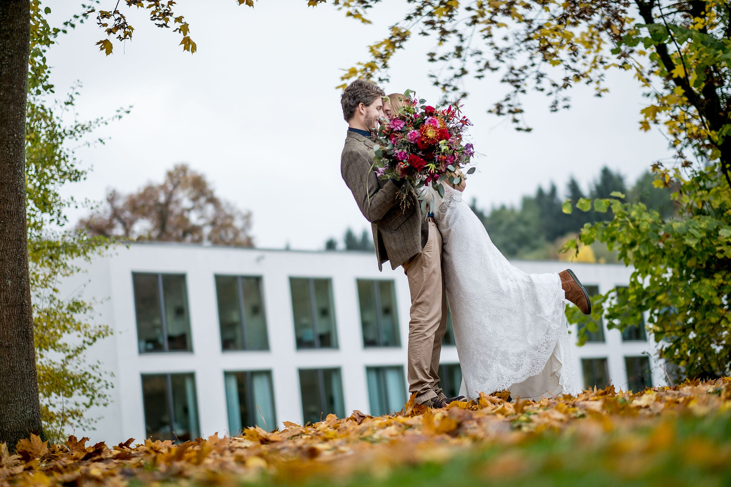 Ein Hochzeitspaar umarmt sich inmitten von bunten Herbstblättern vor dem Hotel FREIgeist Northeim