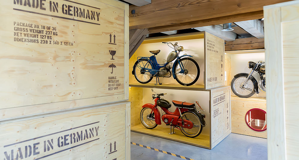 Mehrere Motorräder stehen in Kisten übereinander gestapelt in einer Ausstellungshalle