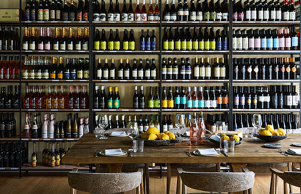 Das große Weinsortiment des Viani Alimentari und eine lange Tafel mit Weingläsern und Zitronen davor
