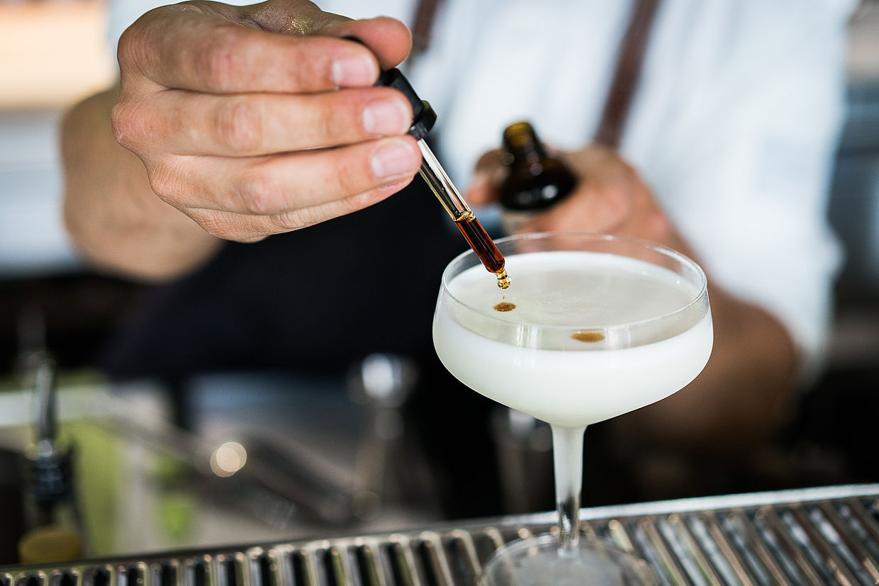 Ein Mitarbeiter tröpfelt Aroma in einen Cocktail in der HERBARIUM Bar im Hotel FREIgeist in Göttingen