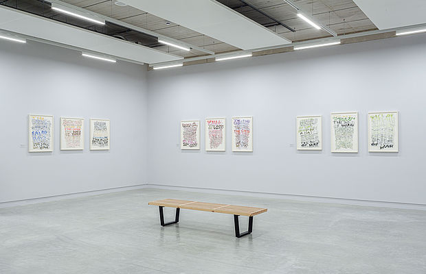 Moderne Ausstellung mit gerahmten Textkunstwerken und Sitzbank.