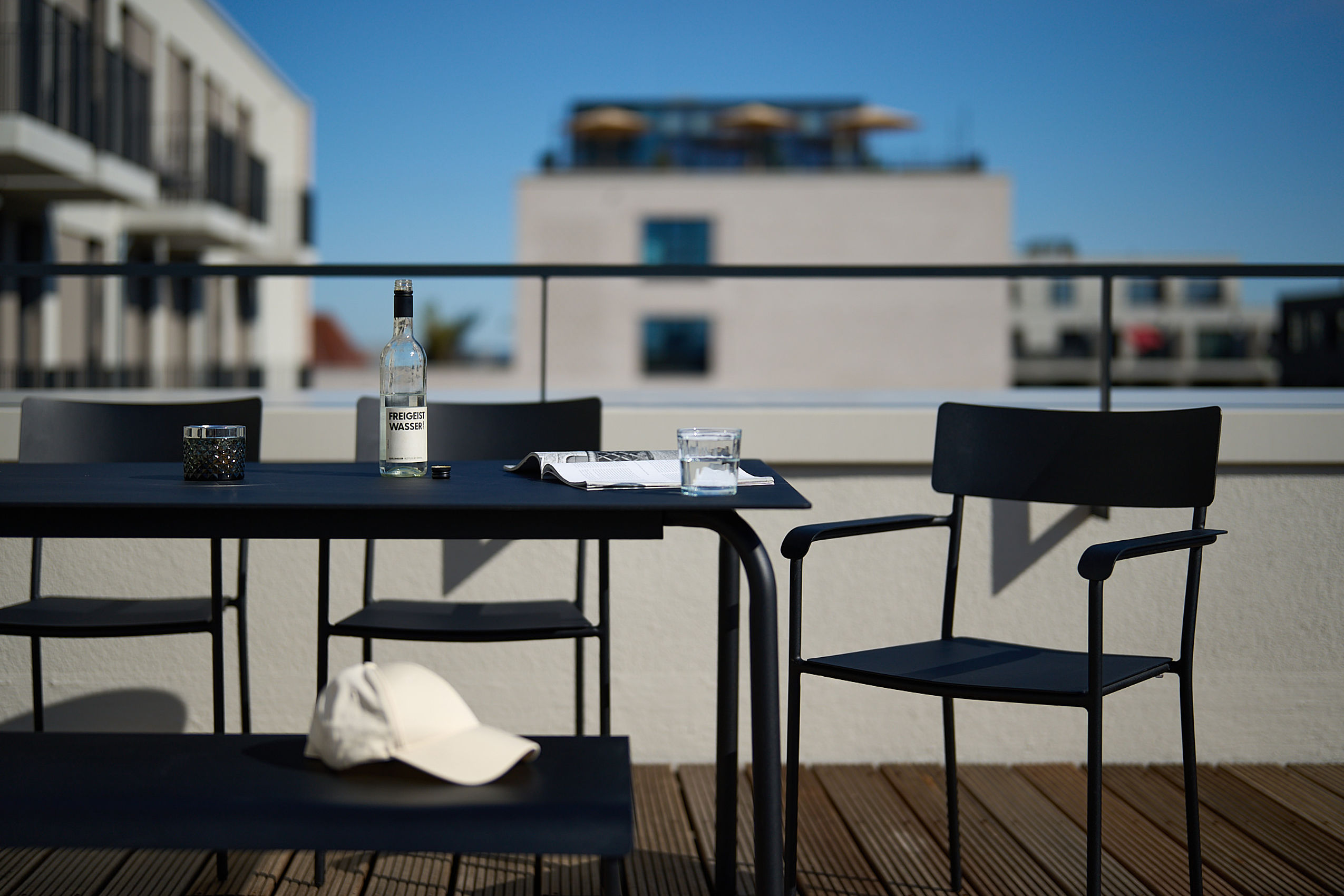Ein moderner, schwarzer Tisch auf der Dachterrasse der FREIgeist Homes mit Wasser und einer Zeitschrift darauf