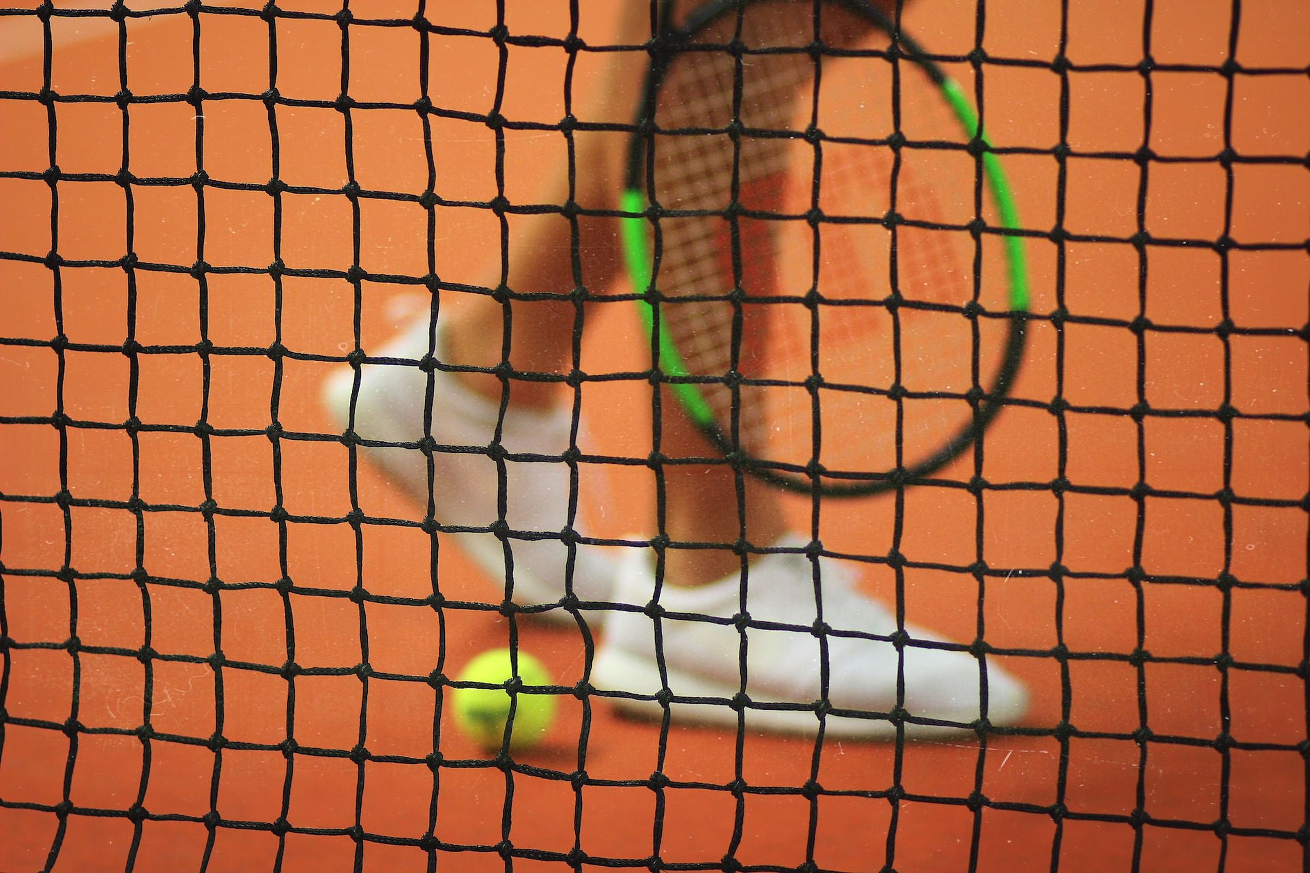 Ein Tennisspieler, ein Schläger und ein Ball hinter einem Tennisnetz auf dem Platz des Hotel FREIgeist Northeim