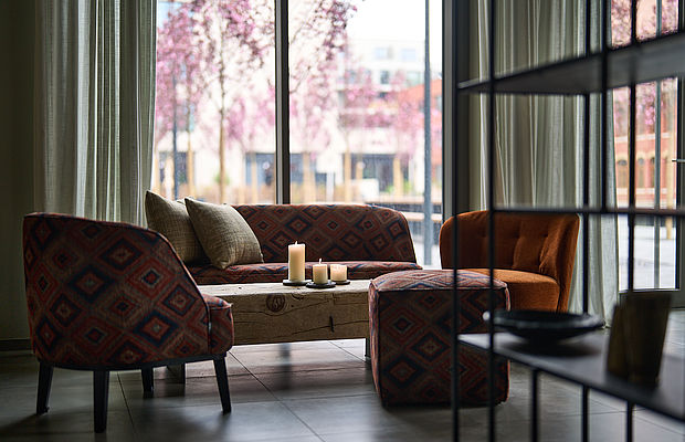 Sitzgruppe mit Kerzen im Lounge-Bereich mit Blick auf Frühlingsbäume.