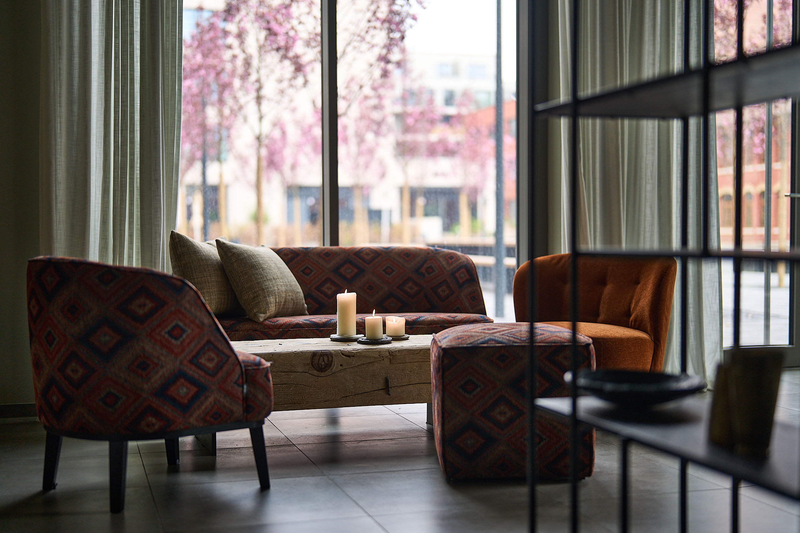 Sitzgruppe mit Kerzen im Lounge-Bereich mit Blick auf Frühlingsbäume.
