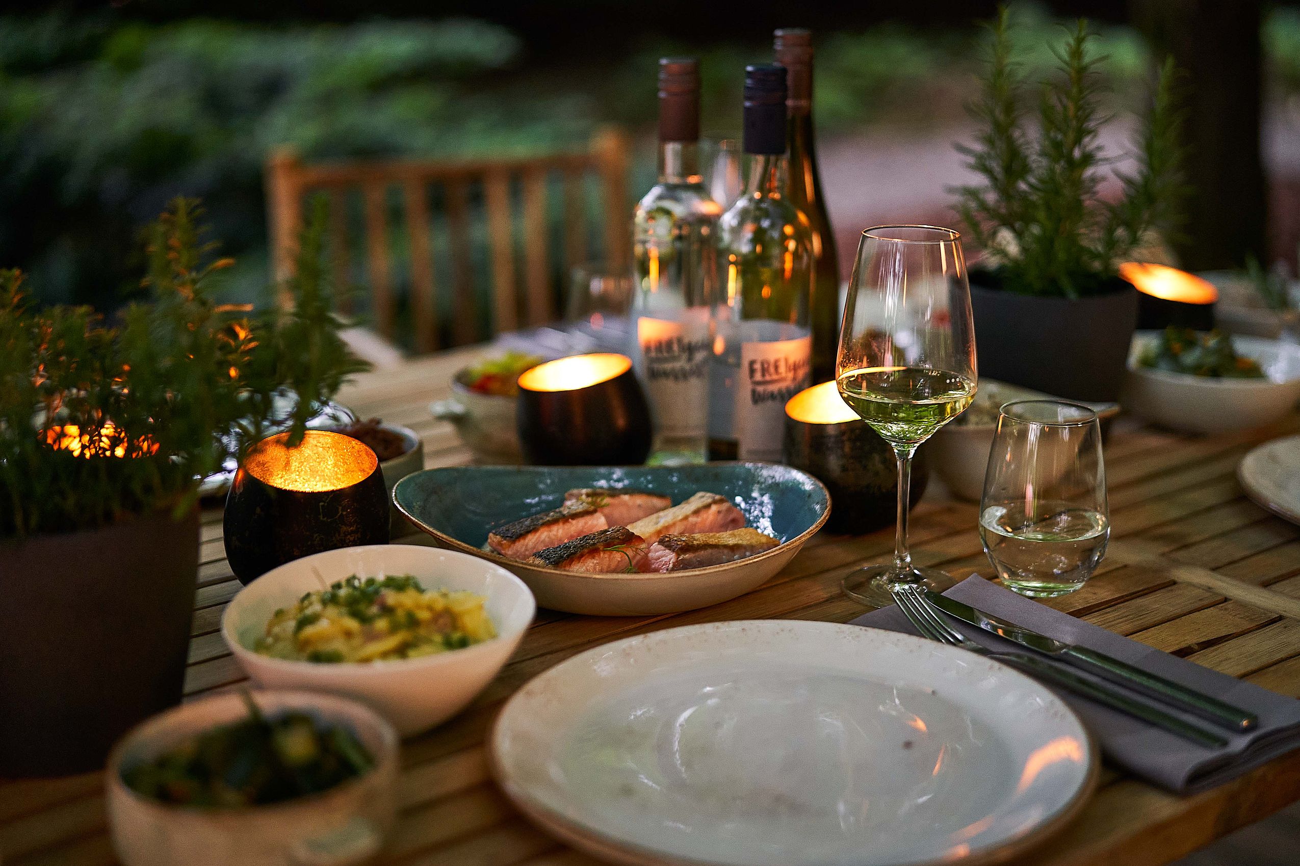 Gebratener Lachs und ein Glas Weißwein auf einem von Kerzen beleuchteten Tisch