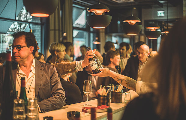 Ein Barkeeper übergibt 2 Flaschen Bier an eine Person in der Menge