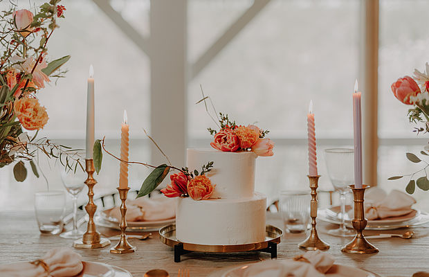Eine Nahaufnahme einer Hochzeitstorte mit orangefarbenen Blumen, daneben Kerzen und Dekorationen