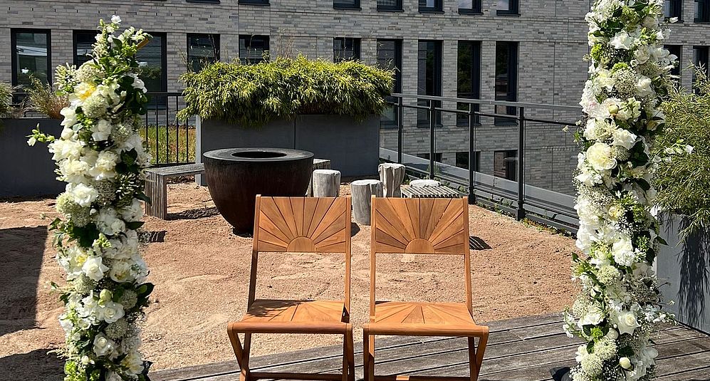 Zeremonienbereich mit Stühlen und Blumenbogen auf moderner Dachterrasse.