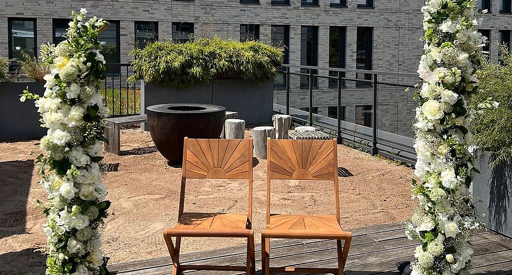Zeremonienbereich mit Stühlen und Blumenbogen auf moderner Dachterrasse.