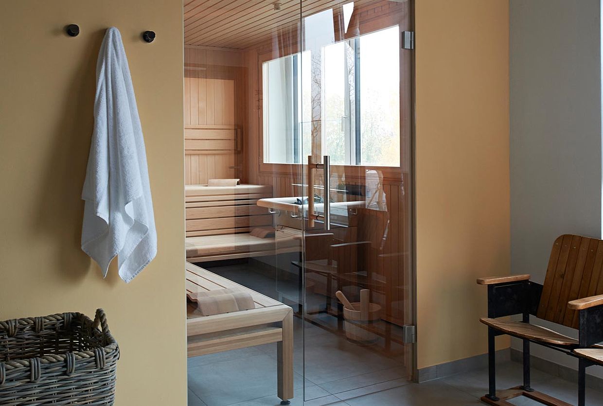 Im Hotel mit Saune in Niedersachen hängt vor einer Sauna ein Handtuch an der Wand und steht ein Bast Korb auf dem Boden